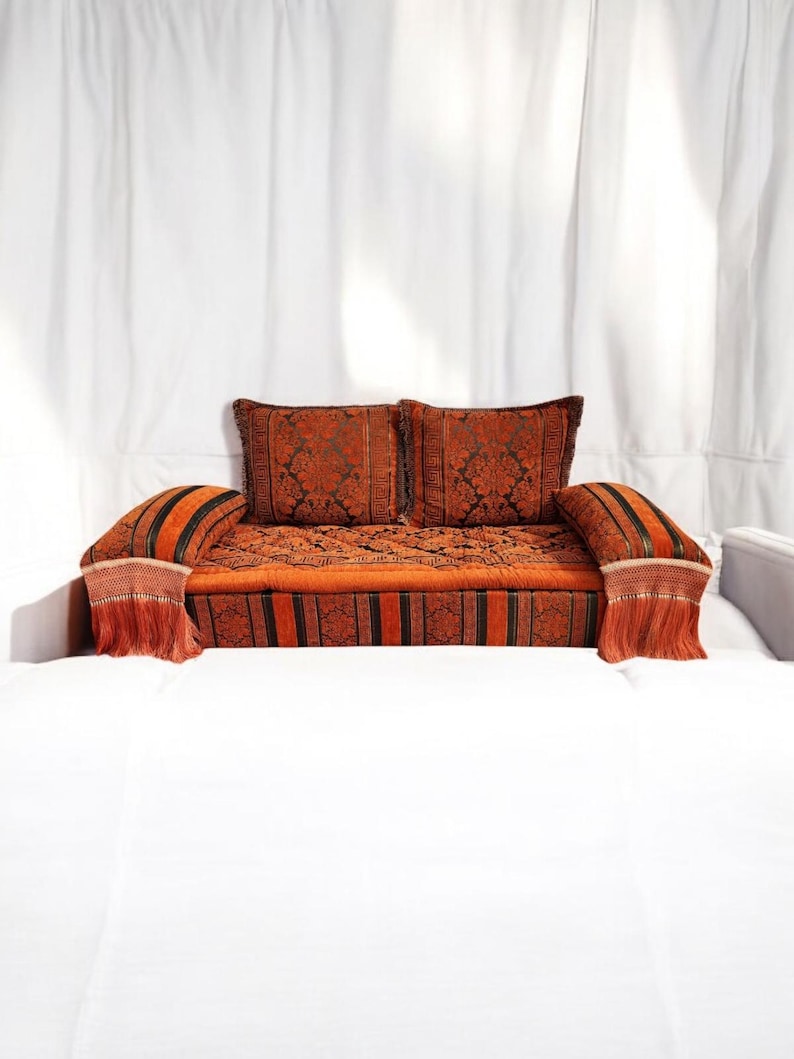 May include: A traditional Moroccan sofa with a rich orange and black patterned fabric. The sofa has two cushions and armrests with tassels.