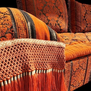 May include: A large orange and black patterned sofa with a crocheted fringe trim. The sofa has a tufted back and seat cushions.