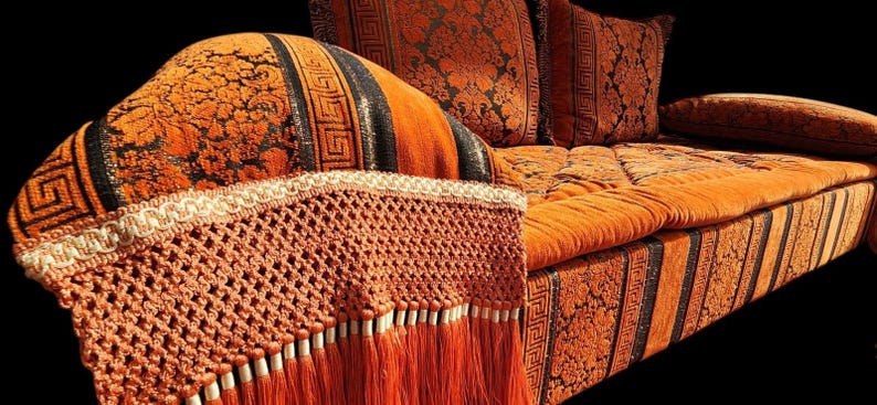 May include: A large orange and black patterned sofa with a crocheted fringe trim. The sofa has a tufted back and seat cushions.