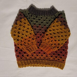 Könnte beinhalten: Ein handgefertigter Häkelpullover in einem Farbverlauf aus Gold, Orange, Braun und Grün. Der Pullover hat einen Rundhalsausschnitt und lange Ärmel. Das offene Webmuster ist im gesamten Kleidungsstück sichtbar.
