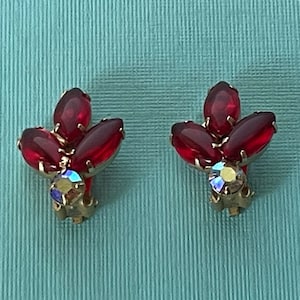 Op de afbeelding: Een paar clip-on oorbellen met een cluster van rode stenen en een enkele heldere strass in het midden van elke oorbel.