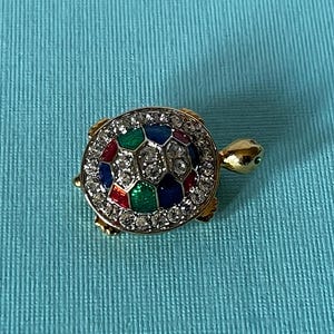 May include: A gold-tone turtle brooch with a colorful enamel shell and clear rhinestones. The shell is decorated with red, green, blue, and yellow enamel.