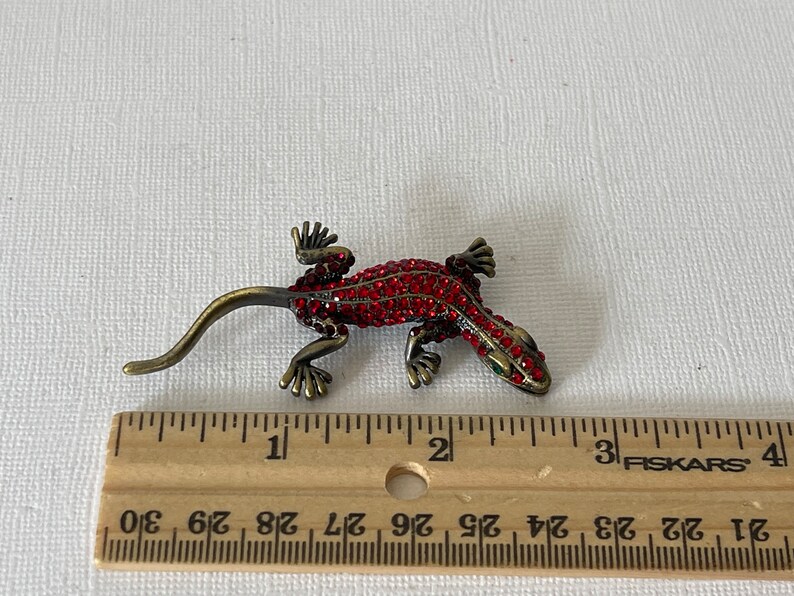 May include: A red jeweled gecko brooch with a gold finish. The brooch is approximately 5 cm long.