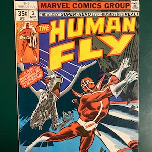 May include: A vintage comic book titled "The Human Fly" from Marvel Comics. The cover features a superhero in a red and white costume in action, with a large yellow title and a detailed illustration of a mechanical bird. The comic book is dated November 1977.