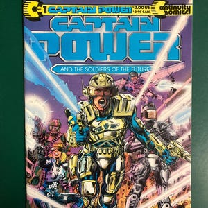 May include: A Captain Power and the Soldiers of the Future comic book issue number 1. The cover features a central armored character in gold and blue gear, surrounded by other soldiers in a battle scene with laser beams and explosions.