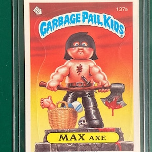 May include: A Garbage Pail Kids trading card featuring "Max Axe." The illustration shows a muscular figure with a black mask, holding an axe with blood dripping from it. A basket, skull, and text "MAX AXE" are also visible.