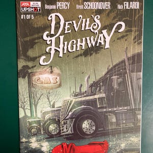 May include: A comic book titled Devil's Highway #1 of 5 featuring a dark, rainy scene with a large semi-truck parked near a gas station sign. A single bright red high-heeled shoe lies on the wet ground in the foreground, surrounded by rain.
