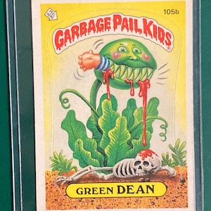 May include: A Garbage Pail Kids trading card featuring a green, plant-like creature with sharp teeth and red blood dripping from its mouth. The card is labeled "Green Dean" and includes a skeleton at the bottom.