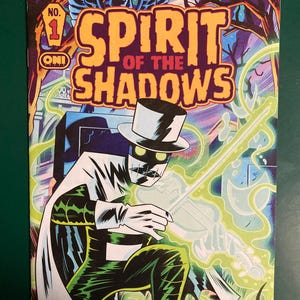 May include: Comic book cover titled "Spirit of the Shadows" with a figure in a top hat and cape playing a glowing violin. The cover features a graveyard scene with a color palette of green, purple, and black. The comic book is labeled "No. 1" and includes the names Daniel Ziegler and Nick Cagnetti.
