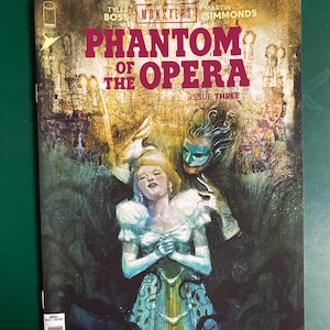 May include: Comic book cover for "Phantom of the Opera" issue three. The cover features a woman in a blue and white dress with a mask and a figure behind her. The title is in large, pink letters.