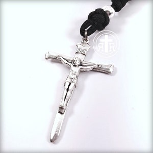 May include: Silver crucifix pendant with a depiction of Jesus Christ on the cross. The inscription "INRI" is visible on the cross. The pendant is attached to a black paracord rosary.