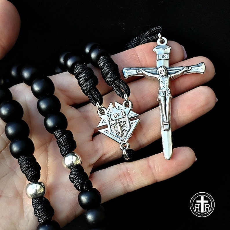 May include: Black rosary beads with a silver crucifix and a silver pendant with the inscription "K of C" on a black cord.