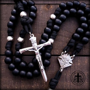 May include: Black rosary beads with a silver crucifix and a silver medal. The crucifix has the inscription "INRI" on the top. The medal has a design of a flower with the inscription "K of C" on it.