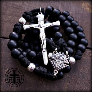 May include: Black rosary beads with a silver crucifix and a silver pendant with the letters "K of C" on it. The crucifix has the inscription "INRI" on it.