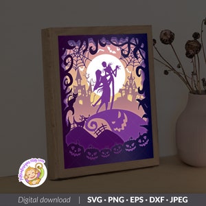 May include: A rectangular light box featuring a layered paper-cut design with a purple and orange color palette. The scene depicts two silhouetted figures standing before a large moon, surrounded by spider webs, a cat, bats, and jack-o'-lanterns.