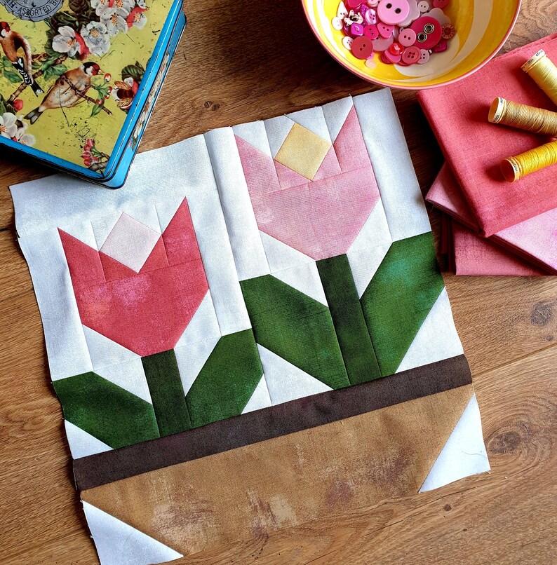 May include: A white fabric panel with two pink and red tulips in a brown pot. The tulips are made of fabric and have green leaves. The fabric panel is perfect for a quilting project.