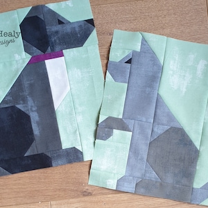 May include: Two fabric patchwork dog designs, one black and gray, the other gray and green. The designs are made of squares and rectangles of different sizes and colors. The designs are on a light wood background.