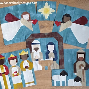 Può includere: Un set di nove quadrati di tessuto che rappresentano una scena della natività. I quadrati sono fatti di tessuto blu, bianco, marrone, rosso e giallo. I quadrati sono disposti in uno schema a griglia su una superficie di legno. I quadrati rappresentano la stella di Betlemme, angeli, i tre re magi, Maria, Giuseppe e un pastore.