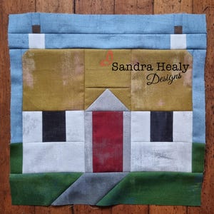 May include: A white cottage with a red door, a thatched roof, and two black windows. The cottage is surrounded by green grass and a blue sky. The text "Sandra Healy Designs" is visible in the upper right corner of the image.