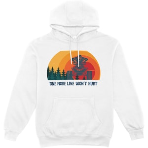 Könnte beinhalten: Ein weißer Kapuzenpullover mit einem Grafikdruck, der eine Person auf einem Quad in einem Wald zeigt. Das Design enthält einen Sonnenuntergangshintergrund in Orange- und Gelbtönen sowie den Text "ONE MORE LINE WON'T HURT" in Dunkelblau.