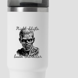 May include: A white stainless steel travel tumbler with a black lid. The front features a black graphic illustration of a zombie face with the text "Night Shifts" above and "build character" below the image in a stylized black script font.