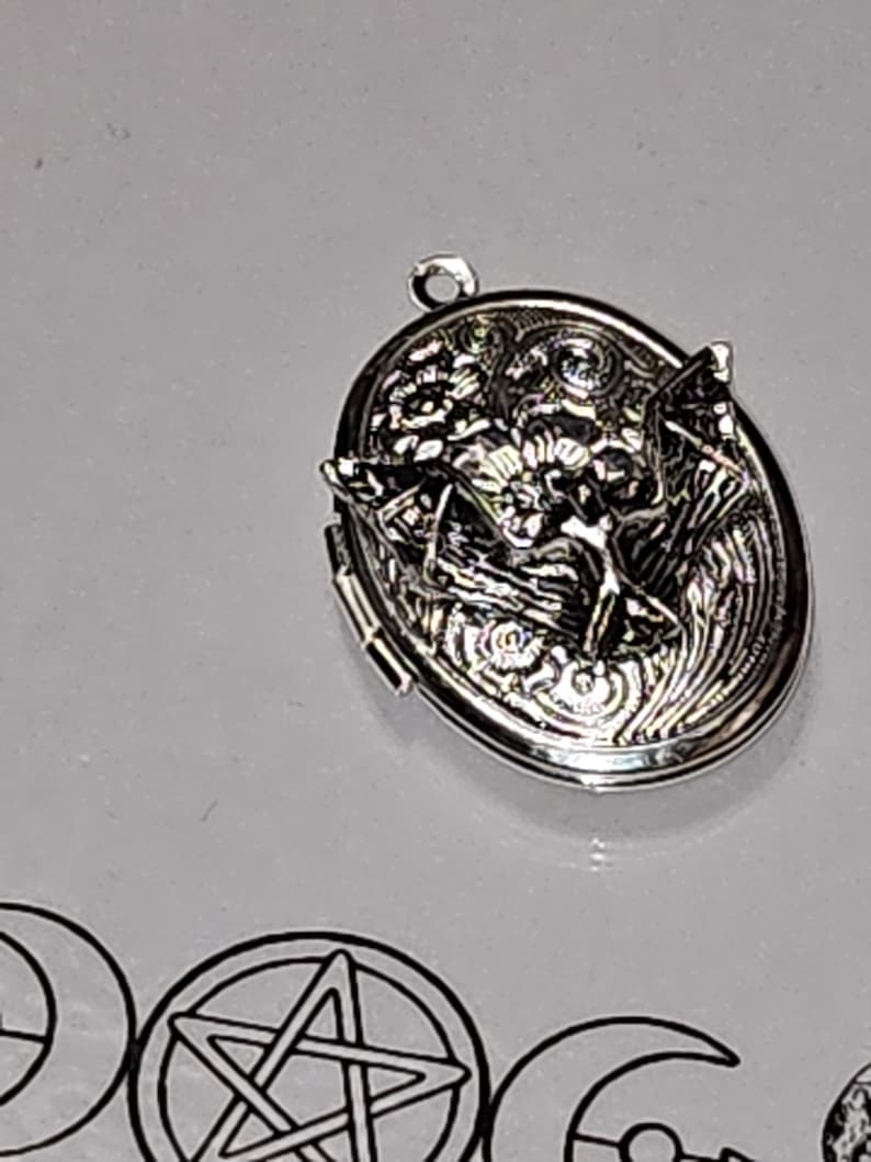 Pu&ograve; includere: Un medaglione ovale in metallo color argento con un design in rilievo raffigurante un pipistrello con le ali spiegate su un motivo floreale. Il medaglione presenta un piccolo anello circolare sulla parte superiore e una chiusura a cerniera.