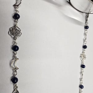 Könnte beinhalten: Eine silberne Kette mit blauen Perlen und silbernen Anhängern, darunter Halbmonde und Rosen, zum Halten von Brillen.