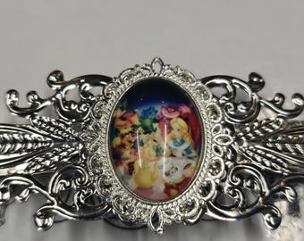 Op de afbeelding: Een zilverkleurige haarclip met een ovaalvormige centrale cabochon. De cabochon toont een kleurrijke illustratie van personages uit Alice in Wonderland tijdens een theekransje. Het metalen frame heeft een ingewikkeld, sierlijk filigraanontwerp.