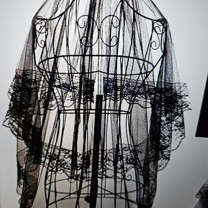 May include: Black lace wedding veil with a scalloped edge, displayed on a mannequin.