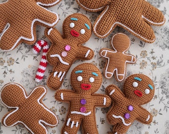 May include: Six crocheted gingerbread people in various sizes and poses. The gingerbread people are brown with white icing details and colorful buttons.