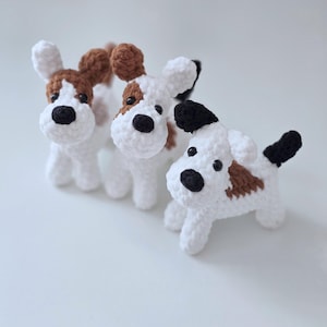 May include: Three crocheted stuffed dog toys. The dogs are white with brown and black markings. The dogs are all different sizes and have different facial expressions.