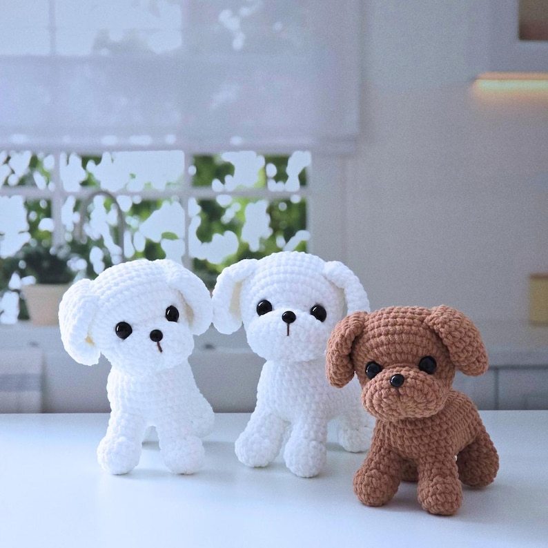 May include: Three crocheted stuffed dog toys. Two are white and one is brown. The white dogs have black eyes and black noses. The brown dog has black eyes and a black nose.