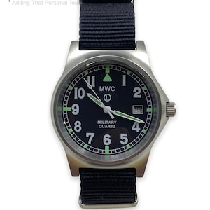 Puede incluir: Un reloj de estilo militar negro con caja plateada y correa de nylon negra. La esfera del reloj tiene n&uacute;meros blancos y una ventana de fecha. La esfera del reloj tambi&eacute;n tiene el texto "MWC" y "MILITARY QUARTZ".