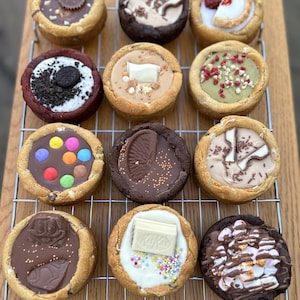 Puede incluir: Una variedad de galletas gourmet con varios ingredientes, incluyendo chocolate, caramelos y crema. Las galletas están dispuestas sobre una rejilla, mostrando una variedad de sabores y diseños. Las galletas están horneadas hasta obtener un color marrón dorado.