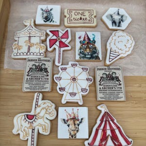 Op de afbeelding: Assortiment van circus-thema koekjes, waaronder een carrousel, een reuzenrad en een giraffe met een kroon. Andere koekjes tonen een zebra, een olifant, een tijger en een ticket. De koekjes zijn versierd met witte glazuur en kleurrijke details.