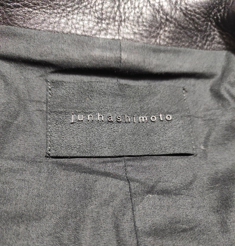 May include: A black leather label with the text "Junhashimoto" in white lettering.