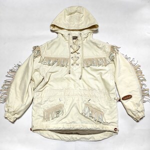 May include: A white hooded jacket with a lace-up front and fringe detailing. The jacket has a brown leather patch with the word "broture" on it.