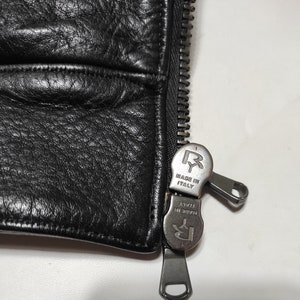 May include: Close-up of a black leather jacket zipper with a silver zipper pull that says "Made in Italy" and has the letter "R" on it.