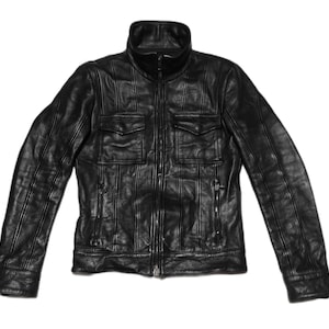 May include: A black leather jacket with a zipper closure and two large flap pockets. The jacket has vertical stitching details throughout.