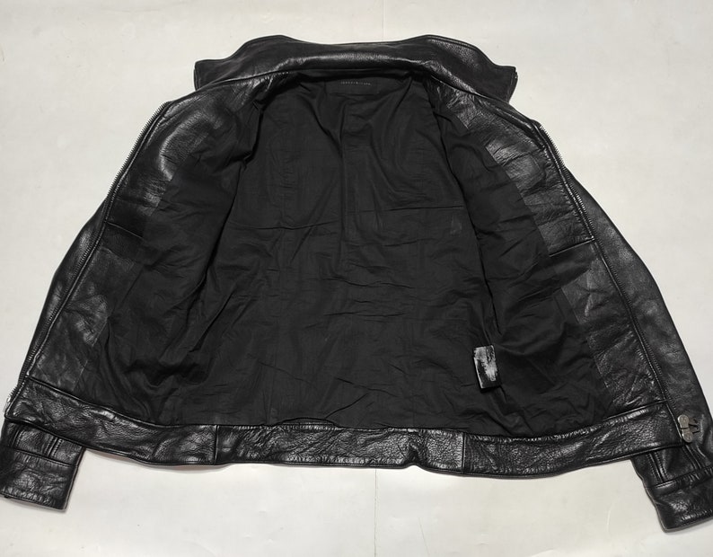 May include: Black leather jacket with a zipper closure and a stand-up collar. The jacket is unlined and has a smooth, soft texture.