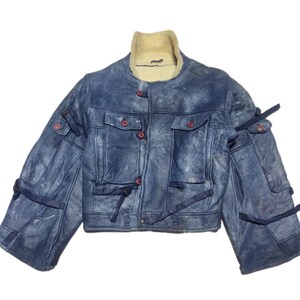 Op de afbeelding: Een blauw spijkerjack met een cr&egrave;mekleurige schapenvachtkraag. De jas heeft rode knopen, meerdere zakken en donkerblauwe bandjes. De mouwen hebben meerdere zakken en bandjes. De jas is een cropped model.