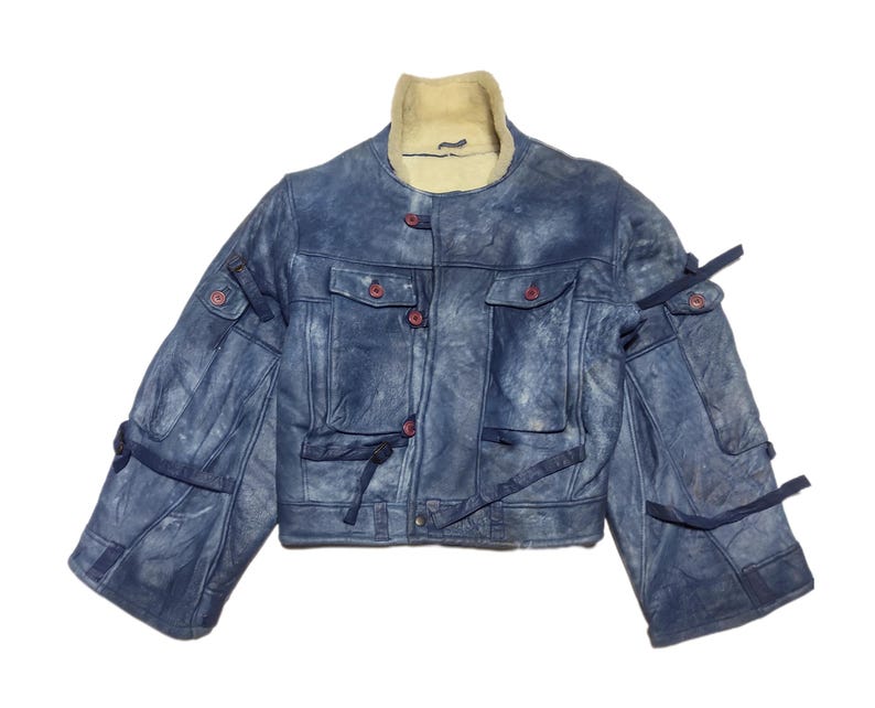 Op de afbeelding: Een blauw spijkerjack met een cr&egrave;mekleurige schapenvachtkraag. De jas heeft rode knopen, meerdere zakken en donkerblauwe bandjes. De mouwen hebben meerdere zakken en bandjes. De jas is een cropped model.