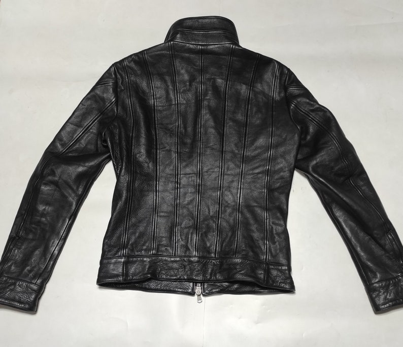 May include: Black leather jacket with a zipper closure and a stand-up collar. The jacket has vertical stitching details on the front and back.