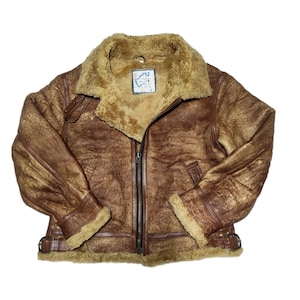 May include: A brown leather bomber jacket with a shearling collar and lining. The jacket has a zipper closure and two pockets. The jacket has a label that says "The Original B-3" on it.