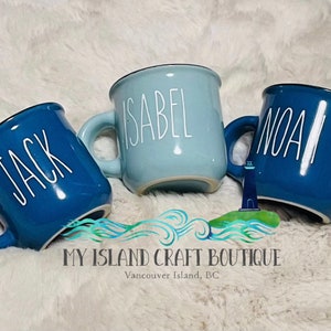 May include: Three ceramic mugs in varying shades of blue, each featuring a white handle and a name printed in white vertical lettering. The left mug is labeled Jack, the center mug is labeled Isabel, and the right mug is labeled Noah.