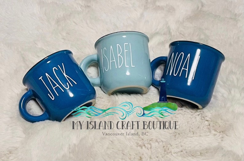 May include: Three ceramic mugs in varying shades of blue, each featuring a white handle and a name printed in white vertical lettering. The left mug is labeled Jack, the center mug is labeled Isabel, and the right mug is labeled Noah.