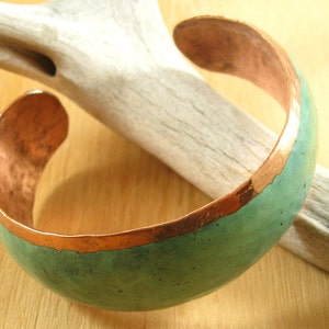 May include: A copper bracelet with a green patina finish. The bracelet is slightly curved and has a smooth, polished surface.