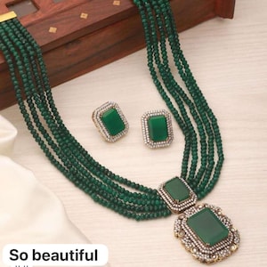 May include: A green beaded necklace with a large emerald green pendant set in gold with white stones. The necklace is layered with multiple strands of beads and comes with matching earrings.