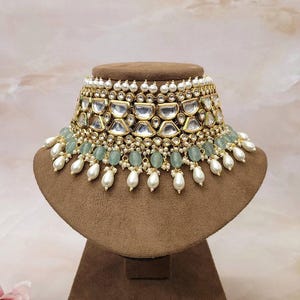 Puede incluir: Un collar gargantilla de oro y plata con un dise&ntilde;o de m&uacute;ltiples capas que presenta perlas blancas, cuentas verdes y piedras transparentes.