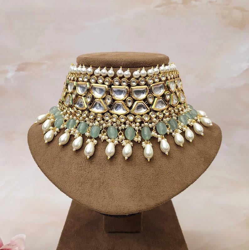 Puede incluir: Un collar gargantilla de oro y plata con un dise&ntilde;o de m&uacute;ltiples capas que presenta perlas blancas, cuentas verdes y piedras transparentes.
